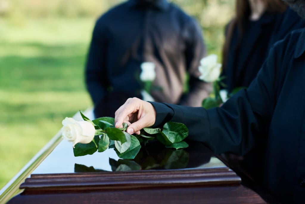 a person holding a white rose on a coffin